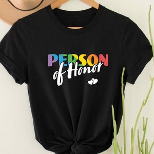 May include: Black t-shirt with the text "PERSON of Honor" in rainbow colors. The text is in a white, handwritten font with two small white hearts below.