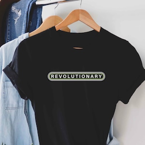 May include: Black t-shirt with a white "REVOLUTIONARY" text in a green and black outlined rectangle.