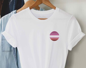 May include: White t-shirt with a pink, white, and purple circle on the left chest. The circle is a representation of the lesbian pride flag.
