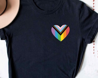 Könnte beinhalten: Schwarzes T-Shirt mit einem Regenbogen-Herz-Design. Das Herz besteht aus verschiedenen farbigen Streifen, darunter Schwarz, Braun, Hellblau, Rosa, Weiß, Gelb, Grün und Orange.