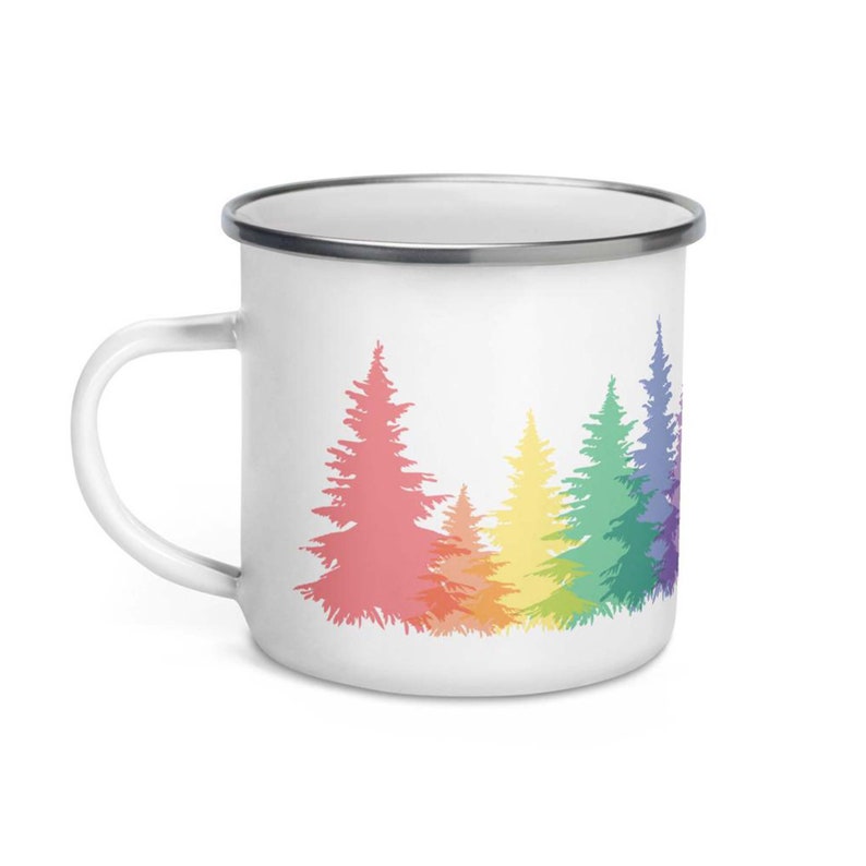 May include: White enamel mug with a rainbow design of pine trees. The trees are outlined in a rainbow pattern, with the colors fading from pink to purple.