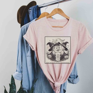 May include: A pink t-shirt with a black and white illustration of two men in witch hats kissing under a full moon. The text "Taking the scenic route on the broomstick" is printed below the illustration.