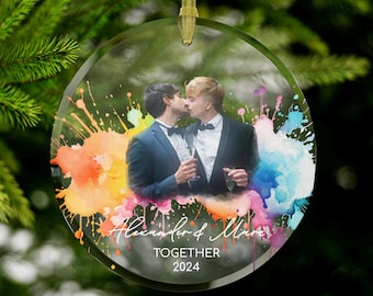 May include: A round glass ornament with a watercolor rainbow splatter design. A photo of two people kissing is in the center of the ornament. The text "Alexander & Marc TOGETHER 2024" is printed on the ornament.