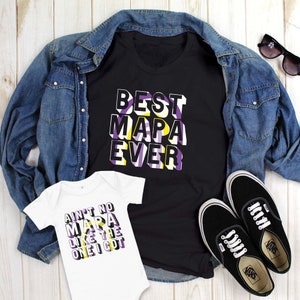 May include: A black t-shirt with the text "BEST MAPA EVER" in white, purple, and yellow. A white baby onesie with the text "AIN'T NO MAPA LIKE THE ONE I GOT" in the same colors. A denim jacket, sunglasses, and black Vans sneakers complete the ensemble.