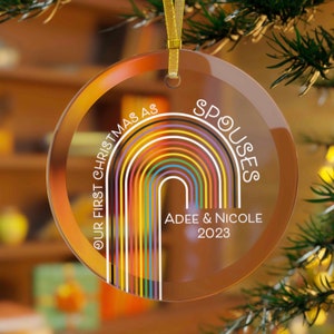 Puede incluir: Un adorno de Navidad de vidrio transparente con un diseño de arcoíris y el texto "Our First Christmas as Spouses Adee & Nicole 2023".