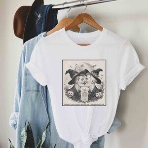 May include: White t-shirt with a black and white illustration of two men in witch hats kissing. The text "Taking the scenic route on the broomstick" is below the illustration.