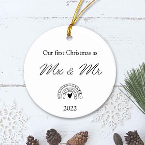 Puede incluir: Adorno navideño de cerámica blanca con texto negro que dice "Nuestra primera Navidad como Mr & Mrs 2022". Debajo del texto hay un arcoíris en blanco y negro con un corazón en el centro.