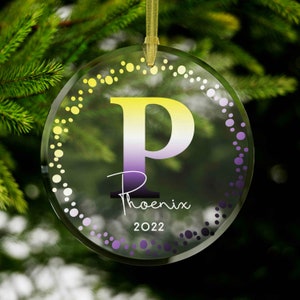 May include: A clear glass Christmas ornament with a yellow, white, and purple gradient letter "P" in the center. The ornament is decorated with a circle of small yellow, white, and purple dots. The text "Phoenix 2022" is printed below the letter.