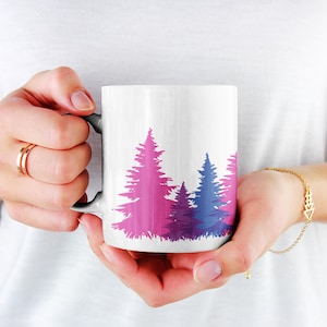 May include: White ceramic mug with a pink, purple, and blue silhouette of a forest of pine trees.