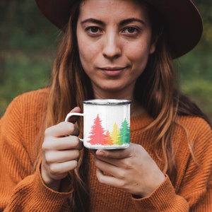 May include: A white enamel mug with a rainbow-colored tree design. The mug has a black rim and handle.