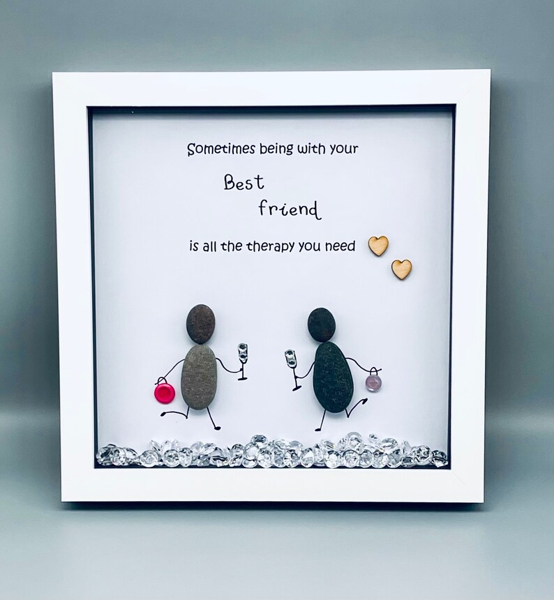 May include: White framed artwork with a hand-painted message that reads "Sometimes being with your best friend is all the therapy you need." The artwork features two stick figures made of stones holding glasses of wine. The stick figures are standing on a bed of rhinestones.