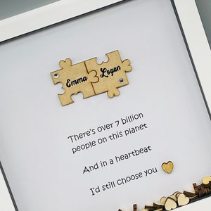 May include: A white frame with a white background and a wooden puzzle piece with the names "Emma" and "Logan" on it. The text "There's over 7 billion people on this planet And in a heartbeat I'd still choose you" is written below the puzzle piece.