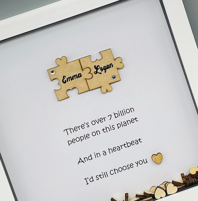 May include: A white frame with a white background and a wooden puzzle piece with the names "Emma" and "Logan" on it. The text "There's over 7 billion people on this planet And in a heartbeat I'd still choose you" is written below the puzzle piece.
