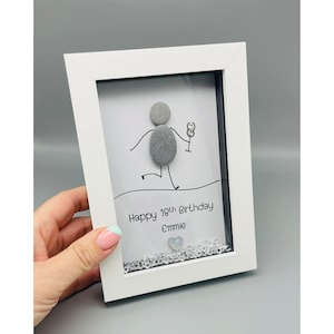 Peut inclure: Cadre blanc avec une &oelig;uvre d'art en galets repr&eacute;sentant une personne tenant un verre. Le texte dit "Happy 18th Birthday Emmie" avec un c&oelig;ur argent&eacute; et des cristaux. Le cadre est tenu par une main.