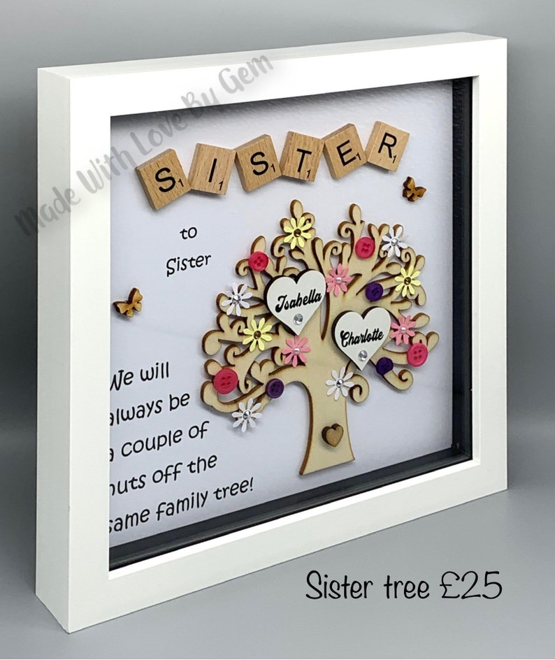 May include: A white framed shadow box with a wooden tree cutout decorated with colorful flowers, buttons, and hearts. The words "Sister" are spelled out with wooden letter tiles. The text "We will always be a couple of nuts off the same family tree!" is written below the tree. The names "Joabella" and "Charlotte" are written on the hearts. The text "Sister tree &pound;25" is written below the frame.