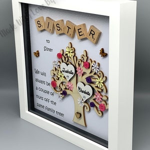May include: A white framed picture with a wooden tree design. The tree has two hearts with the names "Isabella" and "Charlotte" on them. The text "Sister to Sister" and "We will always be a couple of nuts off the same family tree!" is written on the white background.