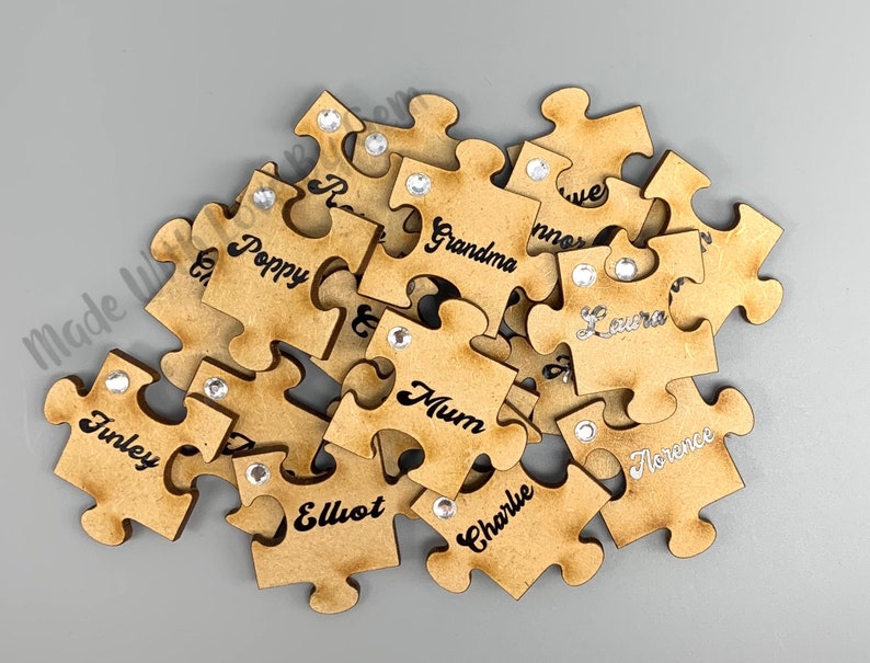 Peut inclure: Un ensemble de pi&egrave;ces de puzzle en bois avec des noms &eacute;crits dessus, dont "Poppy", "Mum", "Grandma", "Elliot", "Finley", "Charlie", "Florence", "Laura", et "Mum". Chaque pi&egrave;ce a un petit strass coll&eacute; dessus.