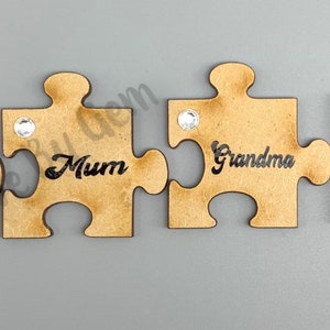 Peut inclure: Quatre pi&egrave;ces de puzzle en bois avec un strass sur chaque pi&egrave;ce. Les pi&egrave;ces sont dispos&eacute;es en rang&eacute;e et chaque pi&egrave;ce porte un nom : Nan, Maman, Grand-m&egrave;re et Mamie.