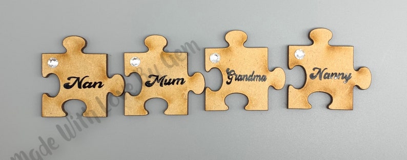 Peut inclure: Quatre pi&egrave;ces de puzzle en bois avec un strass sur chaque pi&egrave;ce. Les pi&egrave;ces sont dispos&eacute;es en rang&eacute;e et chaque pi&egrave;ce porte un nom : Nan, Maman, Grand-m&egrave;re et Mamie.