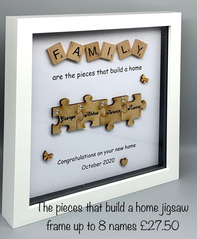 Peut inclure: Un cadre en bois blanc avec un passe-partout blanc et une vitre. Le cadre contient un fond blanc avec le mot "FAMILY" orthographi&eacute; en lettres de bois. Sous le mot "FAMILY" se trouve le texte "are the pieces that build a home". En dessous, il y a un puzzle avec quatre pi&egrave;ces. Chaque pi&egrave;ce porte un nom : "George", "Abbie", "Florence" et "Rose". Sous le puzzle se trouve le texte "Congratulations on your new home October 2020".