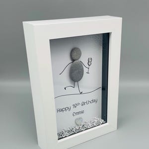 Peut inclure: Cadre blanc avec une &oelig;uvre d'art repr&eacute;sentant une figurine en galets tenant un verre. Le texte "Happy 18th Birthday Emmie" est inscrit. Des cristaux d&eacute;coratifs ornent le bas. Le cadre est inclin&eacute;.