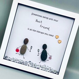 May include: White framed picture with a hand-drawn illustration of two figures made of stones holding glasses. The text reads "Sometimes being with your Best friend is all the therapy you need." Two small wooden hearts are in the top right corner.