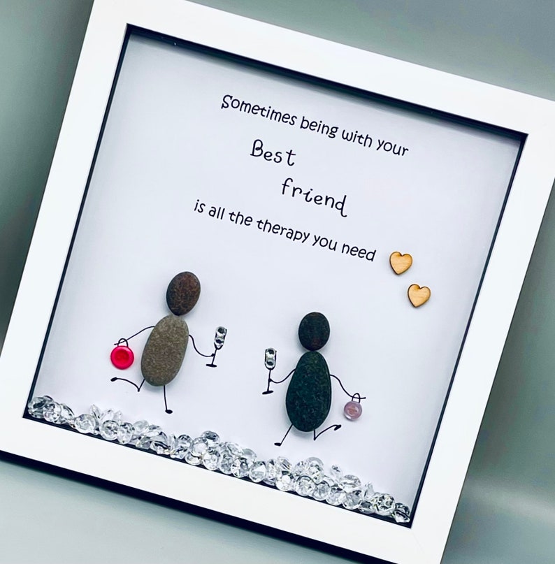 May include: White framed picture with a hand-drawn illustration of two figures made of stones holding glasses. The text reads "Sometimes being with your Best friend is all the therapy you need." Two small wooden hearts are in the top right corner.