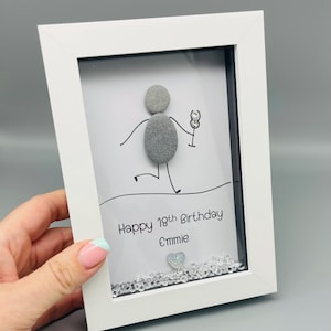Peut inclure: Une &oelig;uvre d'art encadr&eacute;e en blanc avec un personnage en b&acirc;tonnets tenant un verre. Le texte "Happy 18th Birthday Emmie" est en dessous, avec un c&oelig;ur et des cristaux d&eacute;coratifs en bas.