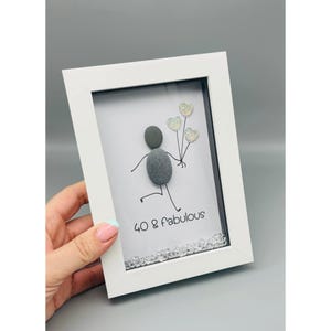 Op de afbeelding: Wit omlijst kunstwerk met een kiezelsteenfiguur die glitter hartballonnen vasthoudt. De tekst luidt "40 & Fabulous". Het kunstwerk is versierd met kleine, heldere kristallen. Een uniek verjaardagscadeau.