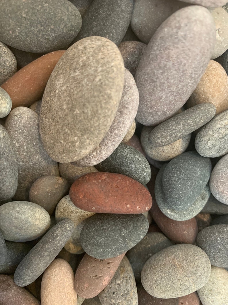 May include: A collection of smooth, oval-shaped stones in various shades of gray, brown, and red. The stones are arranged in a random pattern, creating a natural and textured background.