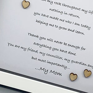 K&ouml;nnte beinhalten: Eine gerahmte Botschaft mit einer handgeschriebenen Nachricht, die einer Mutter Dankbarkeit ausdr&uuml;ckt. Die Nachricht enth&auml;lt die Worte "You have been my rock throughout my life" und "...My Mom". Der Rahmen ist wei&szlig; und hat zwei kleine Holzherzen daran befestigt.
