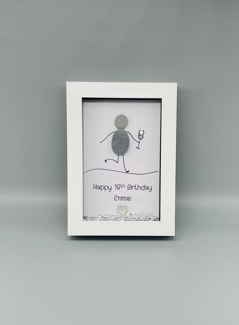 Peut inclure: Cadre blanc contenant une &oelig;uvre d'art avec un personnage en galets tenant un verre &agrave; vin. Le texte dit "Happy 19th Birthday Emmie". Des &eacute;l&eacute;ments d&eacute;coratifs sont pr&eacute;sents en bas.