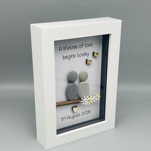 May include: White framed artwork with the text "A lifetime of love begins today." The art features two pebble figures, wooden butterflies, and a date. The frame is white.