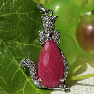 Puede incluir: Colgante de gato plateado con un cuerpo de piedra preciosa roja en forma de lágrima, grande y facetada. La cabeza y la cola del gato están incrustadas con pequeños cristales transparentes. Un lazo de cristales se encuentra en el cuello del gato.