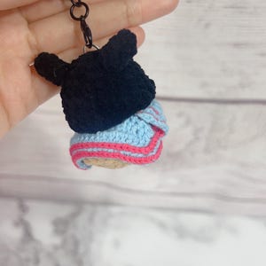 K&ouml;nnte beinhalten: Geh&auml;kelter Schl&uuml;sselanh&auml;nger mit einem schwarzen B&auml;renkopf auf einem blau-rosa geschichteten Design. Der Schl&uuml;sselanh&auml;nger ist an einem schwarzen Metallverschluss und -ring befestigt. Der B&auml;renkopf hat kleine, abgerundete Ohren.