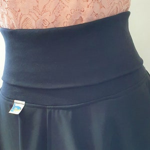May include: A black skirt with a wide waistband and a small label on the front. The skirt is made of a soft, stretchy fabric.