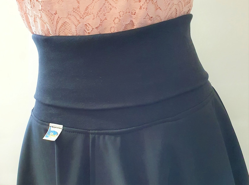 May include: A black skirt with a wide waistband and a small label on the front. The skirt is made of a soft, stretchy fabric.