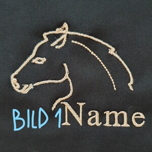 May include: Black fabric with an embroidered outline of a horse's head in tan thread. The text "BILD 1 Name" is written in light blue and tan thread below the horse's head.