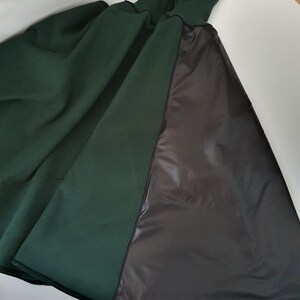 May include: A dark green hooded cape with a black lining. The cape is made of a soft, comfortable fabric and has a relaxed fit.