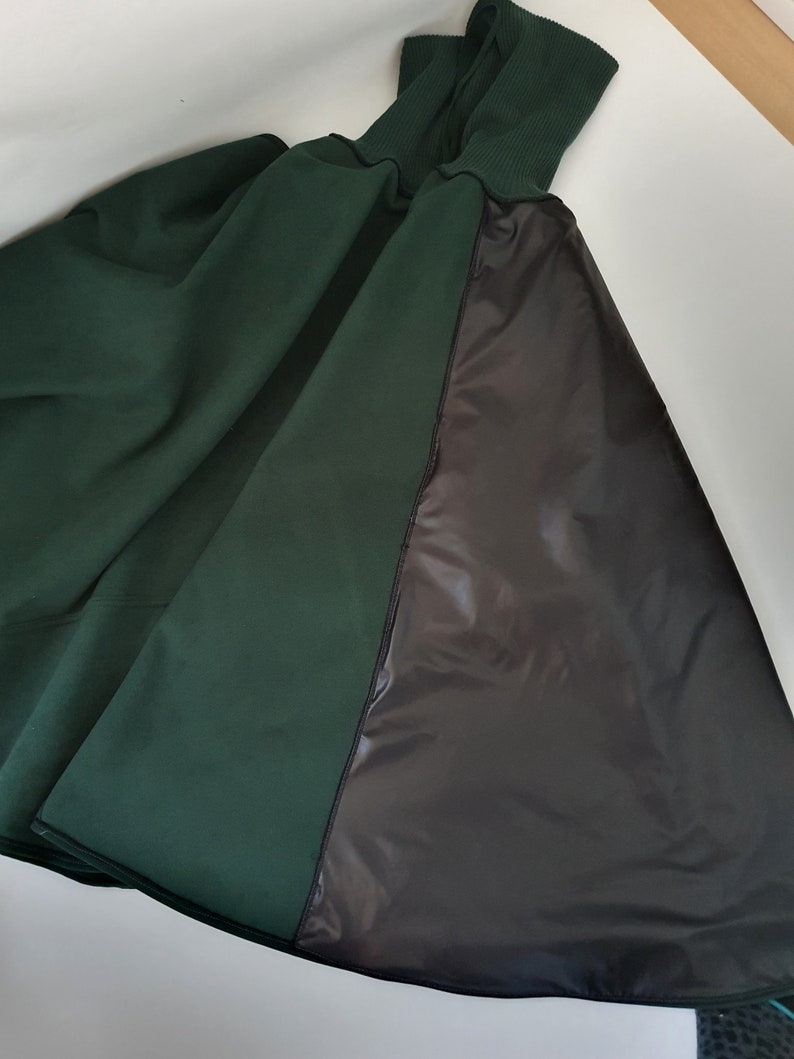 May include: A dark green hooded cape with a black lining. The cape is made of a soft, comfortable fabric and has a relaxed fit.