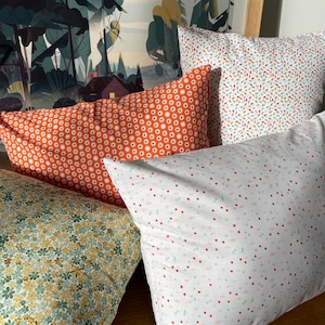 May include: Four throw pillows with different patterns. One pillow has a white background with red, orange, and yellow dots. Another pillow has a white background with small red and green dots. The third pillow has a white background with small orange and blue dots. The fourth pillow has a white background with small red and green dots.