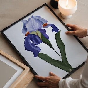 Könnte beinhalten: Ein gerahmter Druck einer blauen und grünen Iris-Blume. Der Druck ist in einem schwarzen Rahmen und wird von den Händen einer Person gehalten.