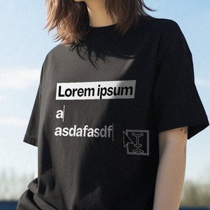 Puede incluir: Una camiseta negra con un diseño gráfico blanco que dice "Lorem ipsum" y "asdafasdf" con un pequeño gráfico de un cuadrado con una flecha apuntando hacia la derecha.
