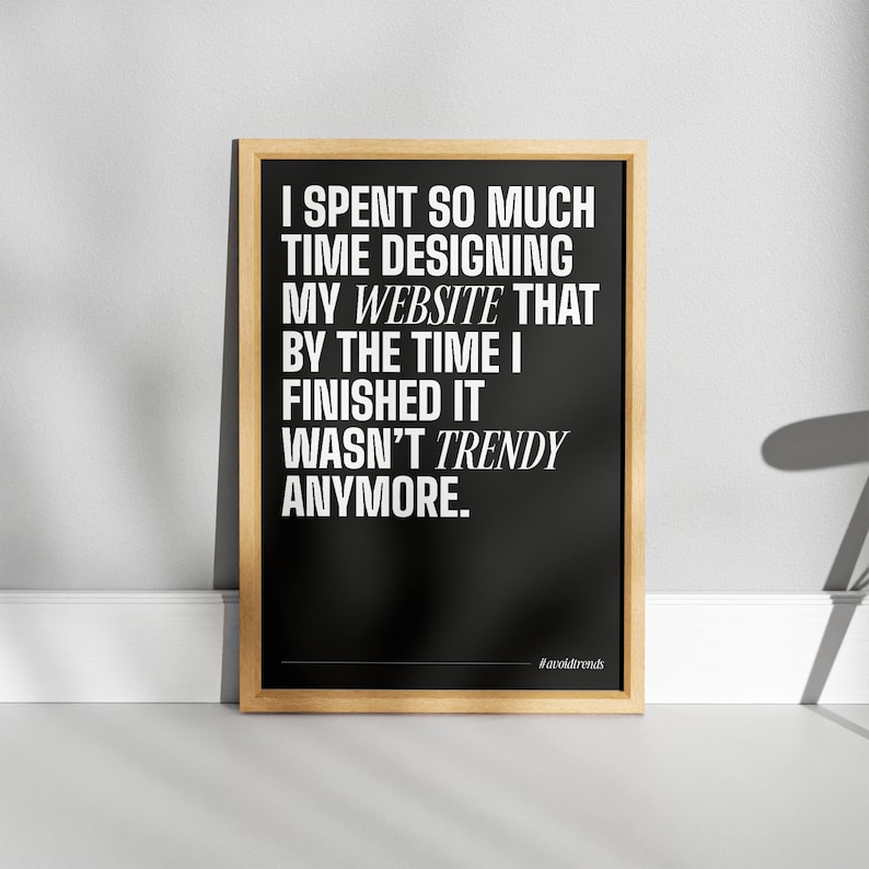 May include: Black and white typography poster with the text "I spent so much time designing my website that by the time I finished it wasn't trendy anymore." The poster has a wooden frame and the hashtag "#avoidtrends" is at the bottom.