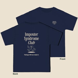 K&ouml;nnte beinhalten: Ein marineblaues T-Shirt mit dem Text "Imposter Syndrome Club" und einer Comicfigur auf der R&uuml;ckseite. Die Vorderseite des Shirts tr&auml;gt den Text "Imposter Syndrome Club" in einer kleineren Schriftart.