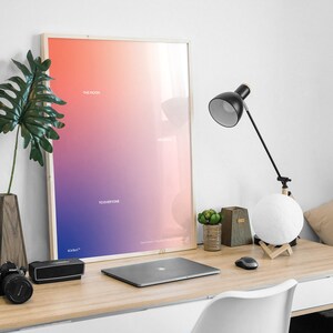 May include: A framed poster with a gradient background of pink, purple, and blue. The poster has the text "The Moon", "Welcome", and "To Everyone" in white. The poster is on a desk with a laptop, a lamp, and a moon lamp.