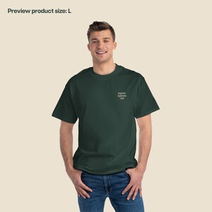K&ouml;nnte beinhalten: Ein dunkelgr&uuml;nes T-Shirt mit dem Text "Imposter Syndrome Club" auf der Brust gestickt.