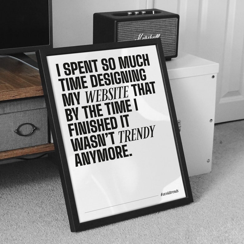 May include: Black and white framed print with a quote about website design. The quote reads "I spent so much time designing my website that by the time I finished it wasn't trendy anymore." The hashtag #avoidtrends is at the bottom of the print.