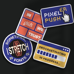 May include: Four colorful stickers with different designs. The first sticker is blue with white text that says "PIXEL PUSH ER". The second sticker is orange and blue with the text "IN grids WE TRUST". The third sticker is blue with white text that says "SOMETIMES... I STRETCH FONTS 88". The fourth sticker is yellow with blue text that says "PROCRASTINATING" and a progress bar that is almost full.