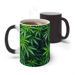 May include: A black and white color-changing mug with a green marijuana leaf pattern on the white side. The mug is filled with coffee.